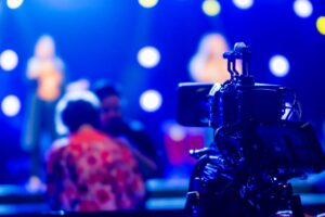 Close-up of a video camera filming a vibrant concert stage with colorful lighting effects.